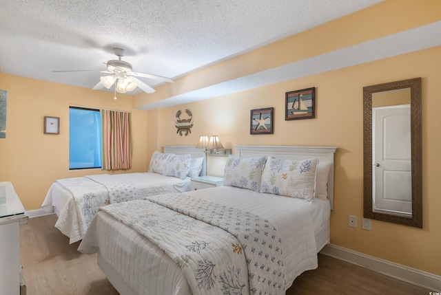 bedroom featuring ceiling fan, a textured ceiling, baseboards, and wood finished floors