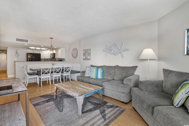 living area featuring a textured ceiling, a chandelier, visible vents, and light wood-style floors