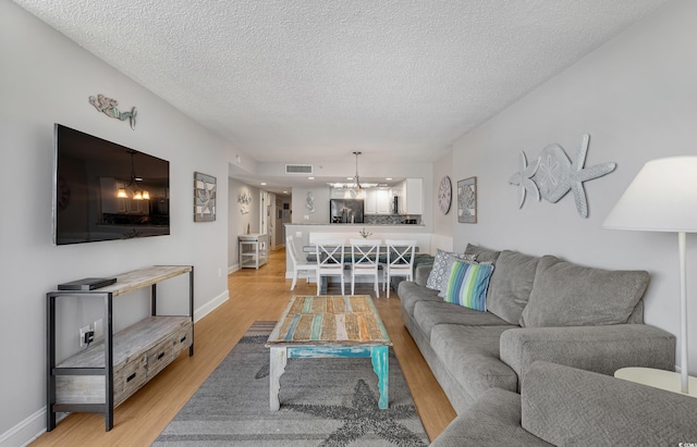 living room with a textured ceiling, a chandelier, visible vents, baseboards, and light wood finished floors