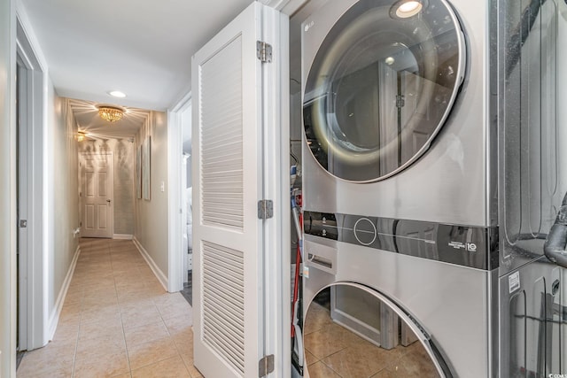 clothes washing area featuring baseboards, laundry area, light tile patterned flooring, and stacked washer / drying machine