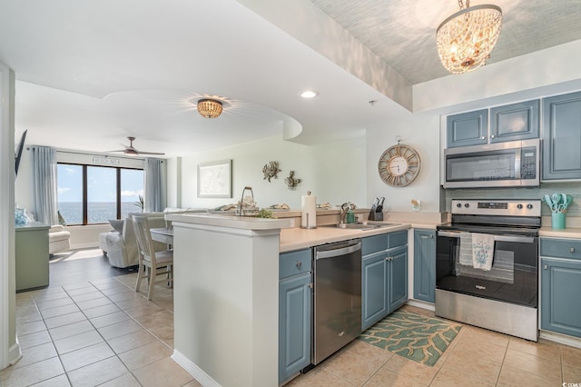 kitchen with a water view, stainless steel appliances, light countertops, a sink, and light tile patterned flooring