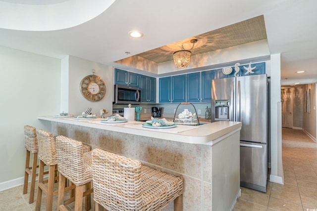 kitchen featuring light countertops, appliances with stainless steel finishes, blue cabinets, a peninsula, and a kitchen bar