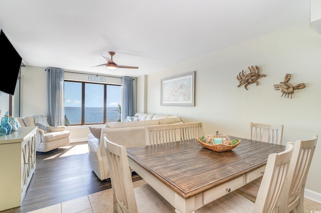 dining space featuring a water view, light wood-style flooring, baseboards, and a ceiling fan