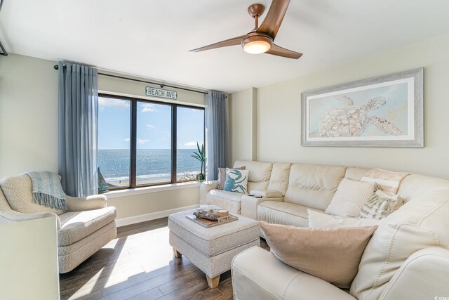 living area featuring a water view, baseboards, a ceiling fan, and dark wood-type flooring