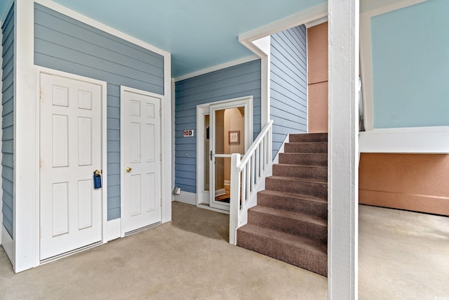 foyer featuring wood walls, stairway, and light colored carpet