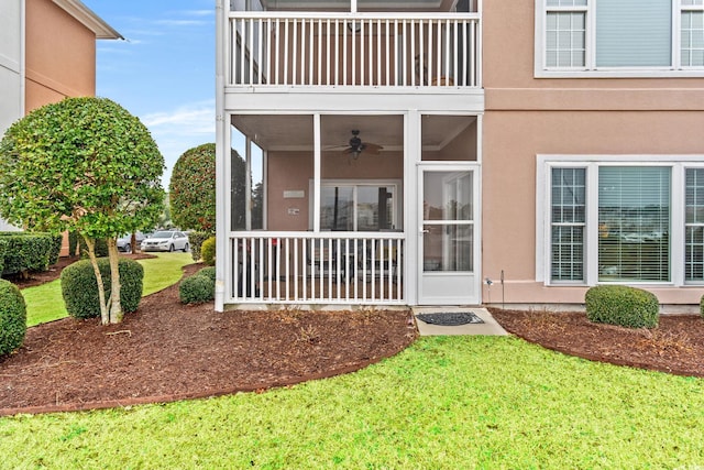 property entrance with a yard, a ceiling fan, and stucco siding