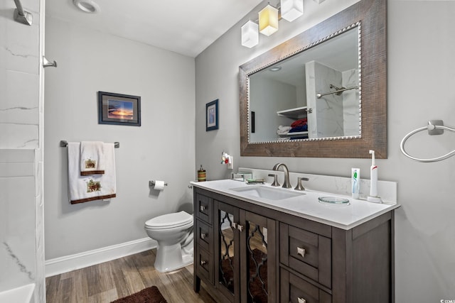 bathroom featuring a shower, toilet, vanity, wood finished floors, and baseboards