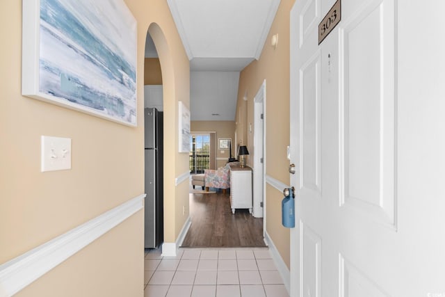 hallway with light tile patterned floors, arched walkways, and baseboards