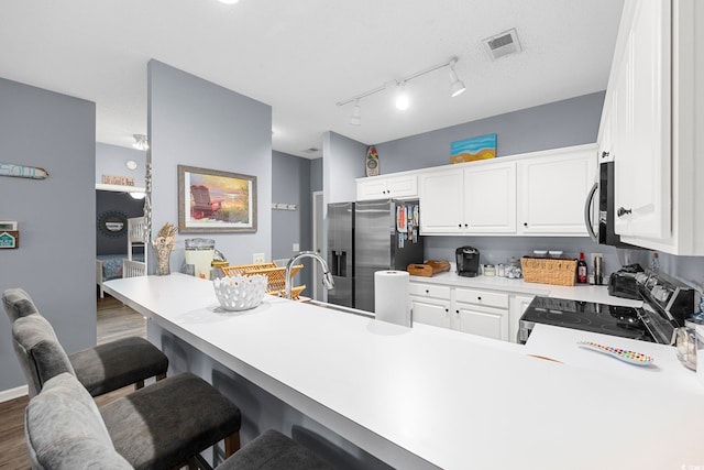 kitchen with a peninsula, stainless steel appliances, white cabinetry, visible vents, and light countertops