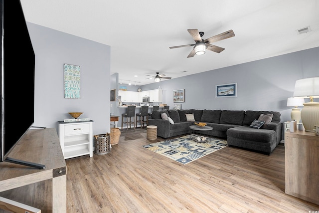 living area featuring light wood-style floors, visible vents, and a ceiling fan