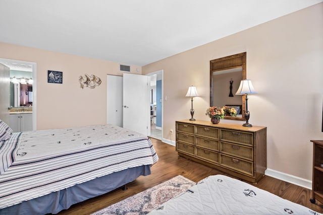 bedroom featuring ensuite bathroom, a sink, visible vents, baseboards, and dark wood-style floors