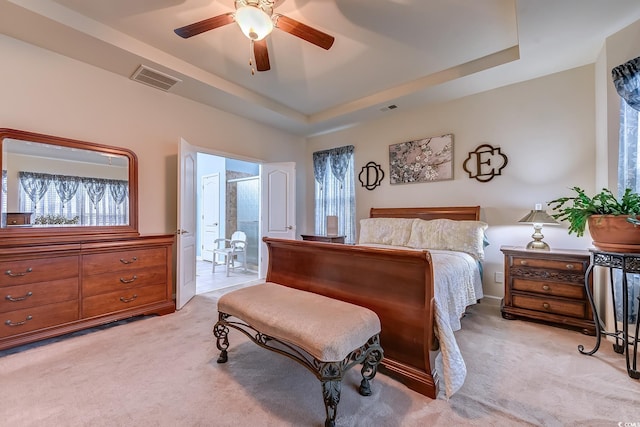 bedroom featuring a tray ceiling, a ceiling fan, visible vents, and light colored carpet