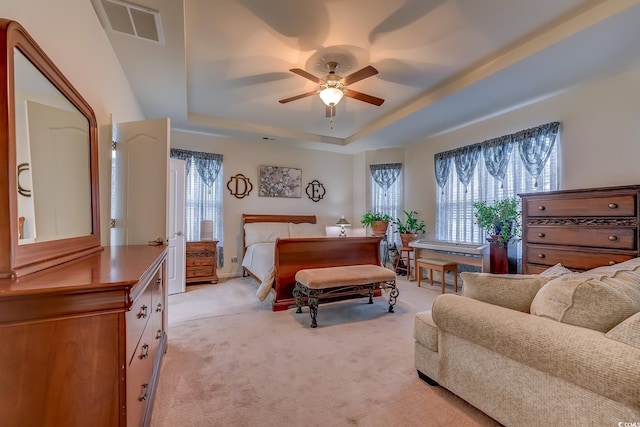 bedroom featuring multiple windows, visible vents, a raised ceiling, and light colored carpet