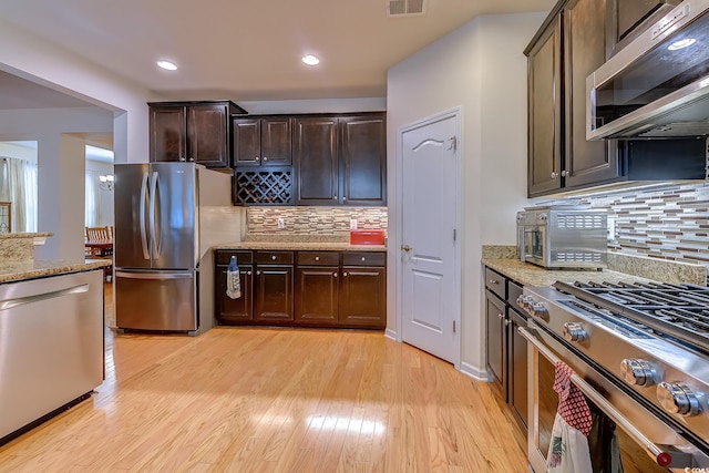 kitchen with stainless steel appliances, light wood-style floors, dark brown cabinetry, and light stone counters