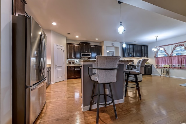 kitchen with dark brown cabinetry, a kitchen island, stainless steel appliances, light wood-style floors, and pendant lighting