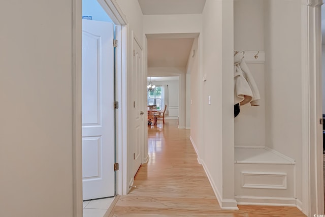 hallway with light wood finished floors, an inviting chandelier, and baseboards