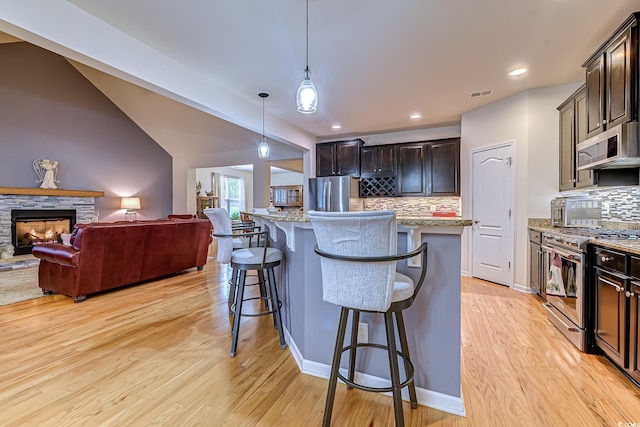 kitchen with light stone counters, dark brown cabinetry, stainless steel appliances, a kitchen breakfast bar, and open floor plan