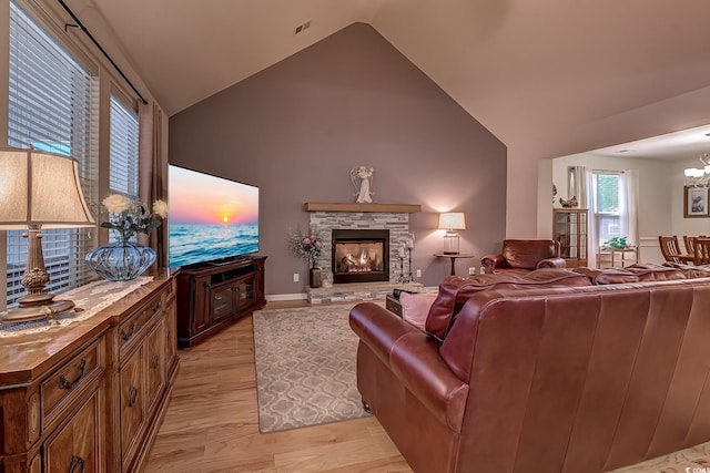 living area featuring visible vents, a stone fireplace, light wood-style floors, high vaulted ceiling, and a notable chandelier