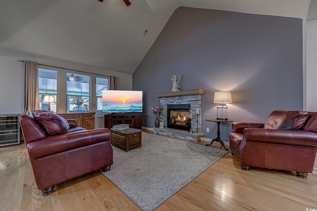 living room with a fireplace, light wood finished floors, visible vents, a ceiling fan, and high vaulted ceiling