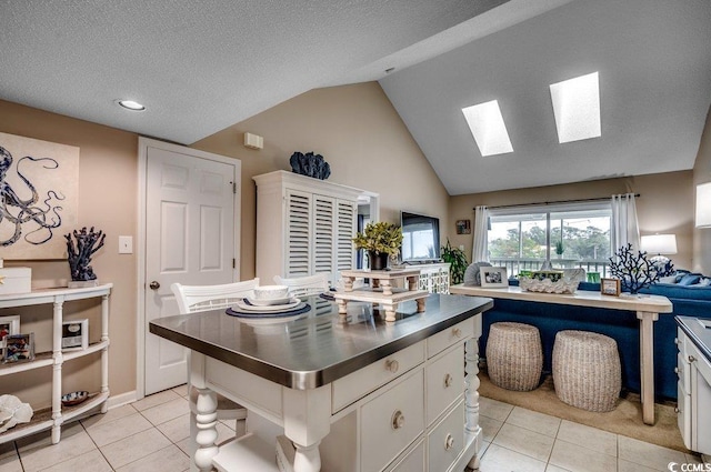 kitchen with vaulted ceiling with skylight, white cabinets, stainless steel countertops, open floor plan, and light tile patterned flooring