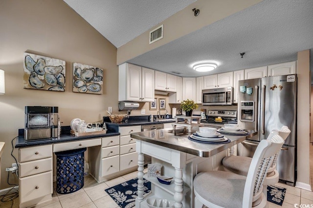 kitchen with light tile patterned floors, a textured ceiling, stainless steel appliances, white cabinets, and dark countertops