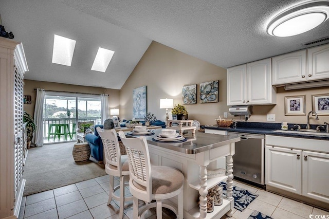 kitchen featuring vaulted ceiling with skylight, visible vents, white cabinets, stainless steel dishwasher, and a sink