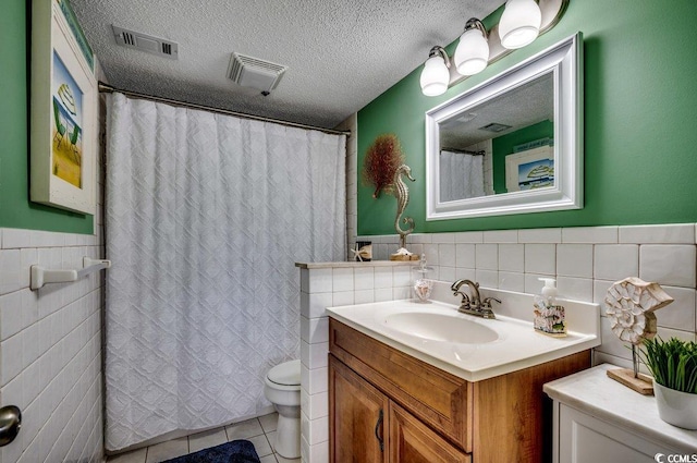 bathroom with a textured ceiling, vanity, visible vents, tile walls, and tile patterned floors