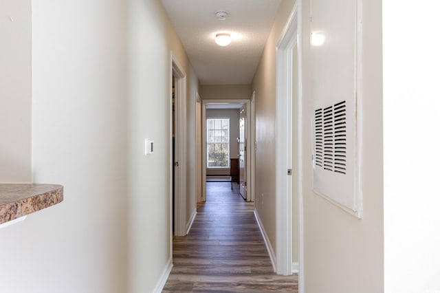 hall featuring a textured ceiling, dark wood-style floors, and baseboards