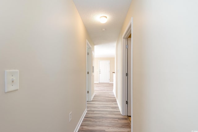 corridor featuring light wood-style floors, a textured ceiling, and baseboards