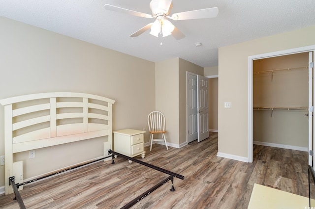 unfurnished bedroom with ceiling fan, a textured ceiling, wood finished floors, baseboards, and a closet