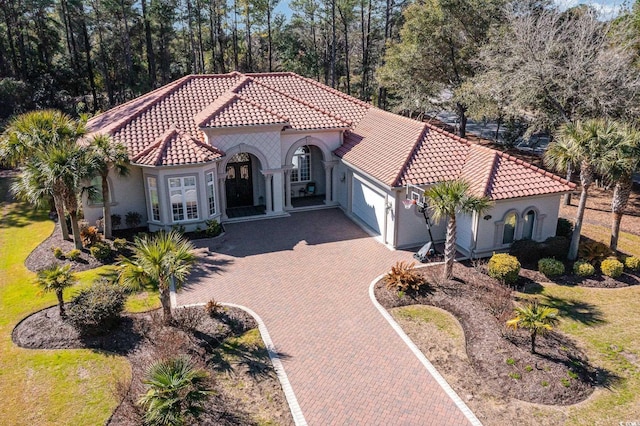 mediterranean / spanish home with decorative driveway, a tile roof, an attached garage, and stucco siding