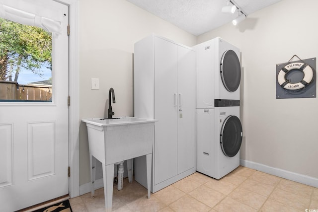 clothes washing area featuring baseboards, laundry area, track lighting, stacked washer and clothes dryer, and a textured ceiling