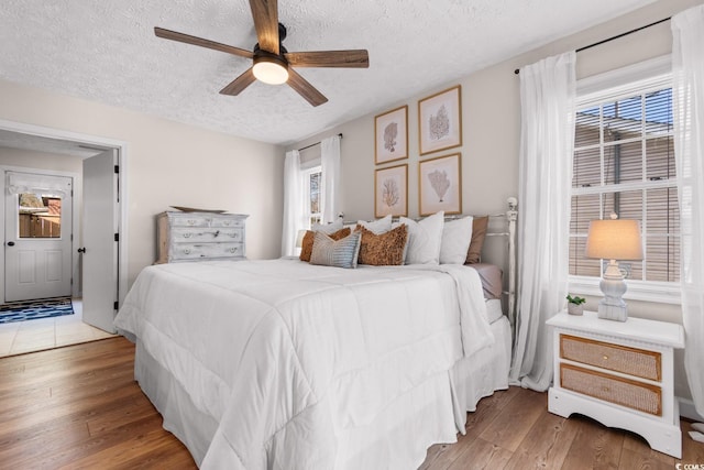 bedroom with light wood-type flooring, a textured ceiling, and a ceiling fan