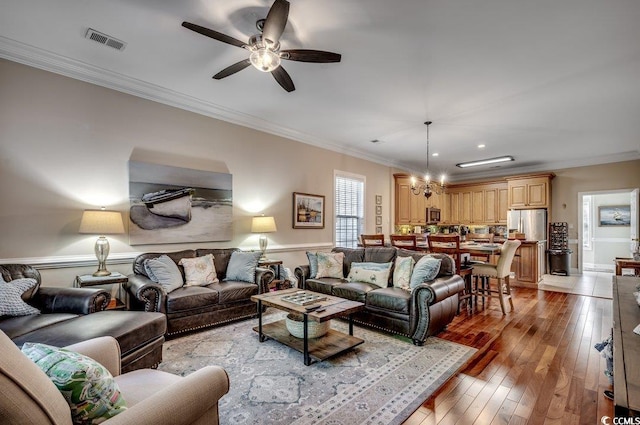 living room with ceiling fan with notable chandelier, light wood-type flooring, visible vents, and crown molding