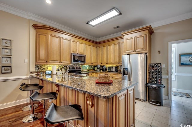 kitchen with a breakfast bar, stainless steel appliances, a sink, dark stone counters, and a peninsula