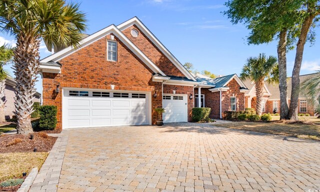 traditional-style home featuring brick siding, decorative driveway, and an attached garage