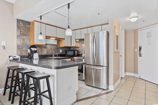 kitchen with dark countertops, hanging light fixtures, a peninsula, stainless steel appliances, and white cabinetry