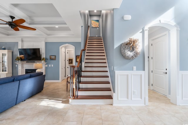 stairway featuring arched walkways, coffered ceiling, a fireplace, a ceiling fan, and decorative columns