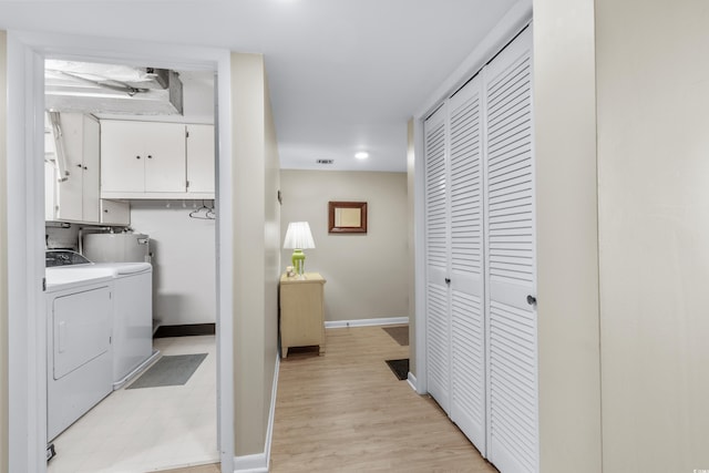 clothes washing area featuring visible vents, baseboards, light wood-style floors, cabinet space, and washing machine and clothes dryer