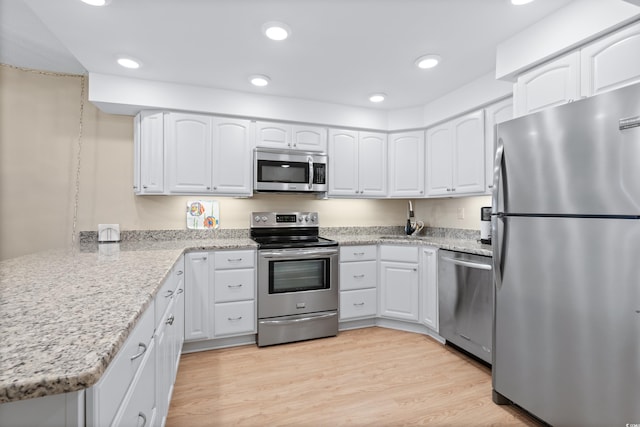 kitchen featuring stainless steel appliances, white cabinets, light wood finished floors, and light stone countertops