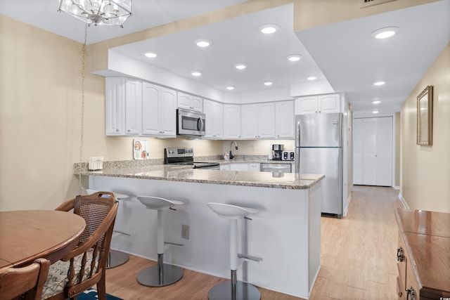 kitchen featuring light wood finished floors, stainless steel appliances, white cabinetry, light stone countertops, and a peninsula