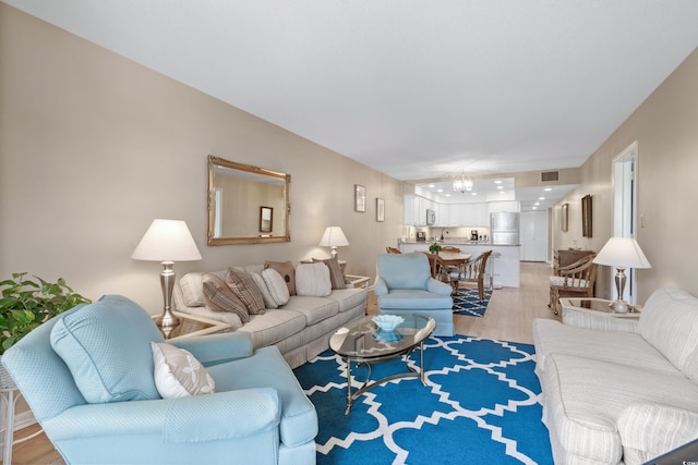 living area featuring visible vents, light wood-style flooring, and a notable chandelier