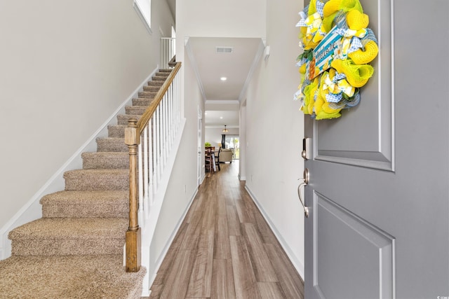 foyer with baseboards, visible vents, wood finished floors, stairs, and crown molding