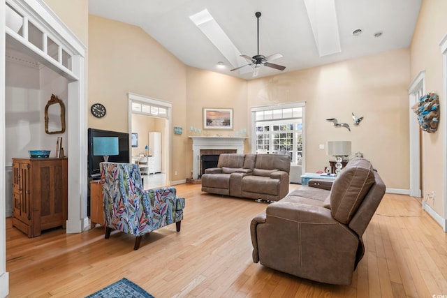 living room with a skylight, light wood-style flooring, baseboards, and a fireplace with raised hearth