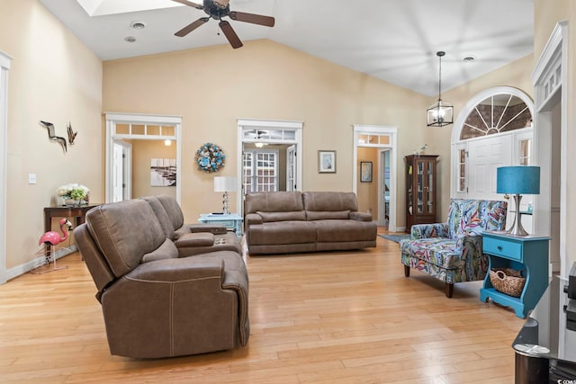 living area with a skylight, light wood-style flooring, high vaulted ceiling, and a ceiling fan