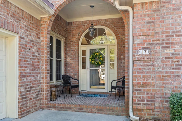 view of exterior entry featuring covered porch, brick siding, and a garage