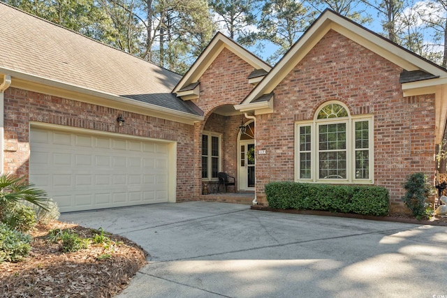 view of front facade with a garage, concrete driveway, brick siding, and roof with shingles