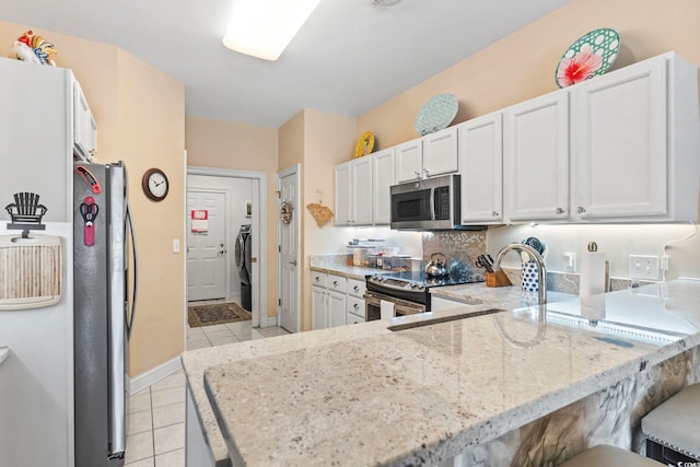 kitchen featuring light tile patterned floors, light stone counters, a peninsula, white cabinets, and appliances with stainless steel finishes