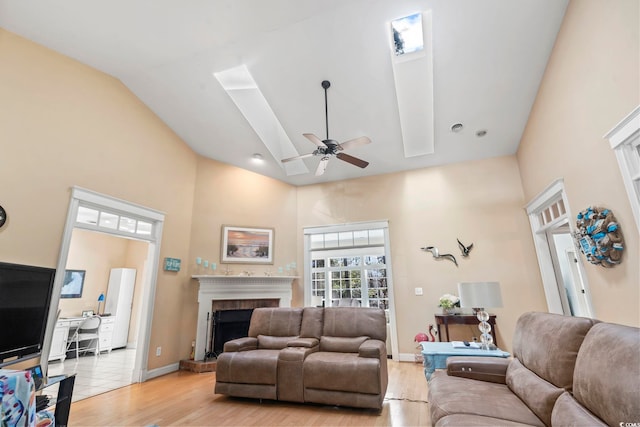 living area featuring a towering ceiling, baseboards, a ceiling fan, a brick fireplace, and light wood finished floors