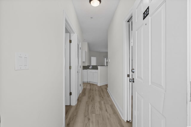 corridor featuring light wood-type flooring and baseboards